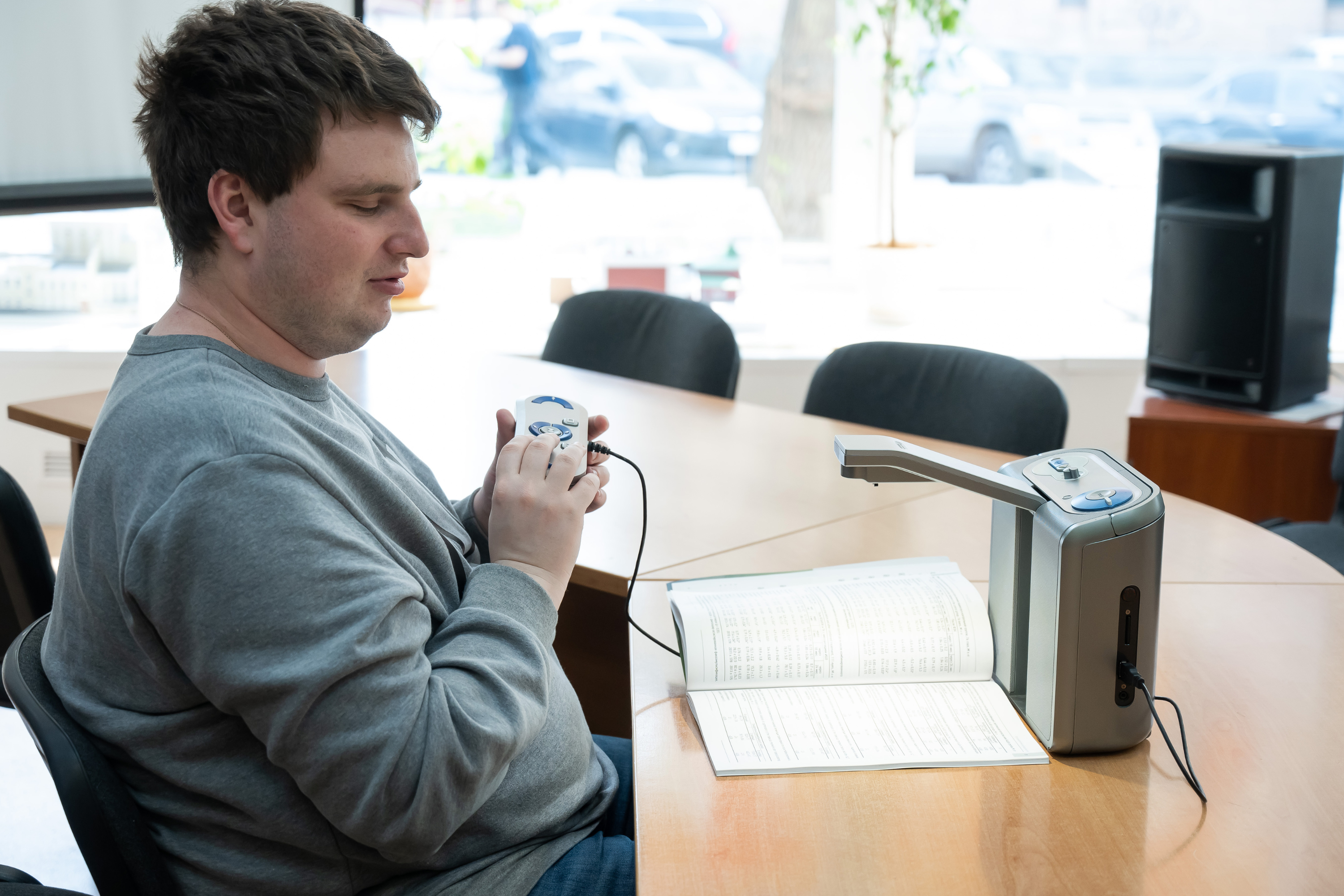 A young man with a visual impairment sat at a desk and using equipment to help read a document.