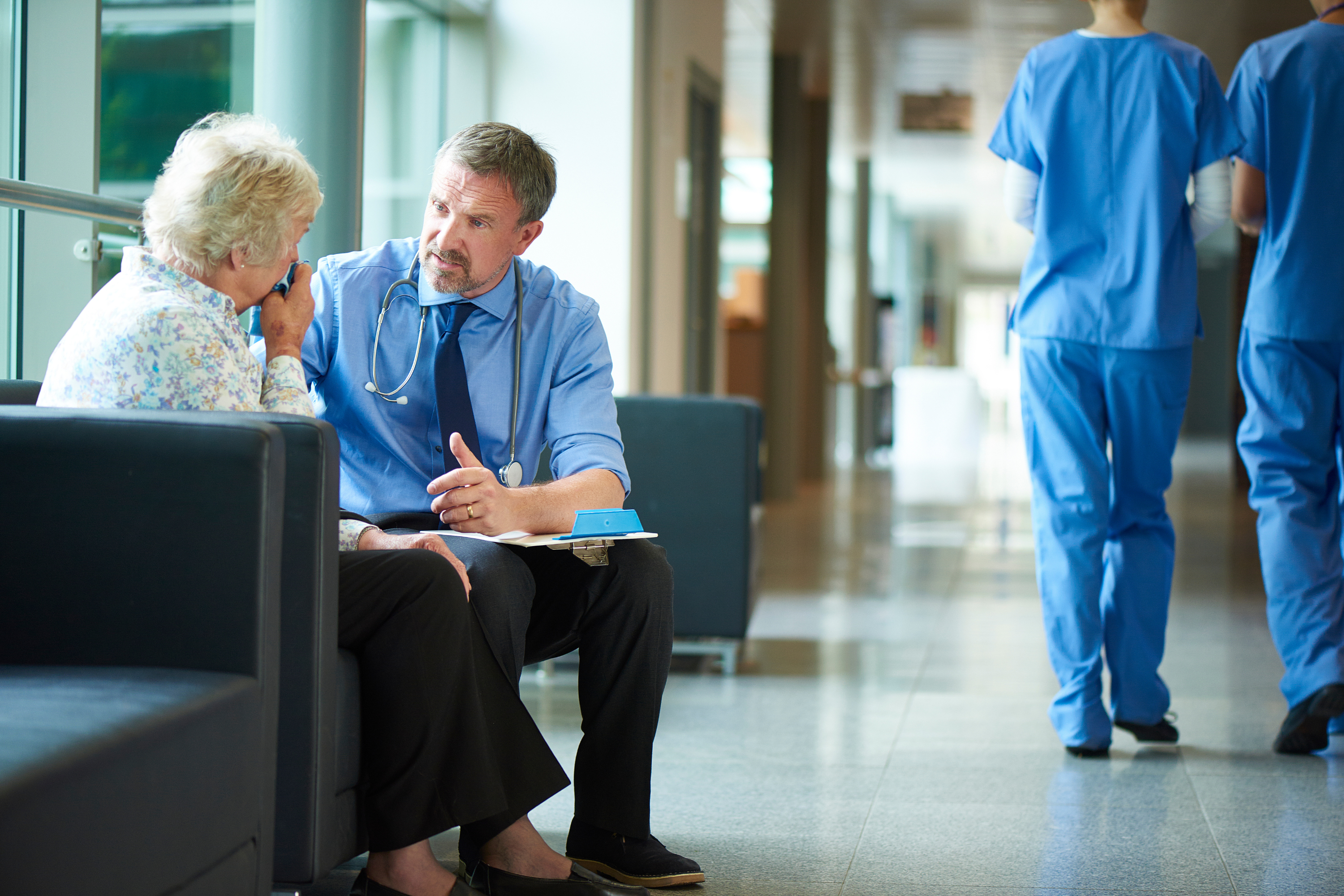 Male doctor talking with a female patient in a hospital corridor.