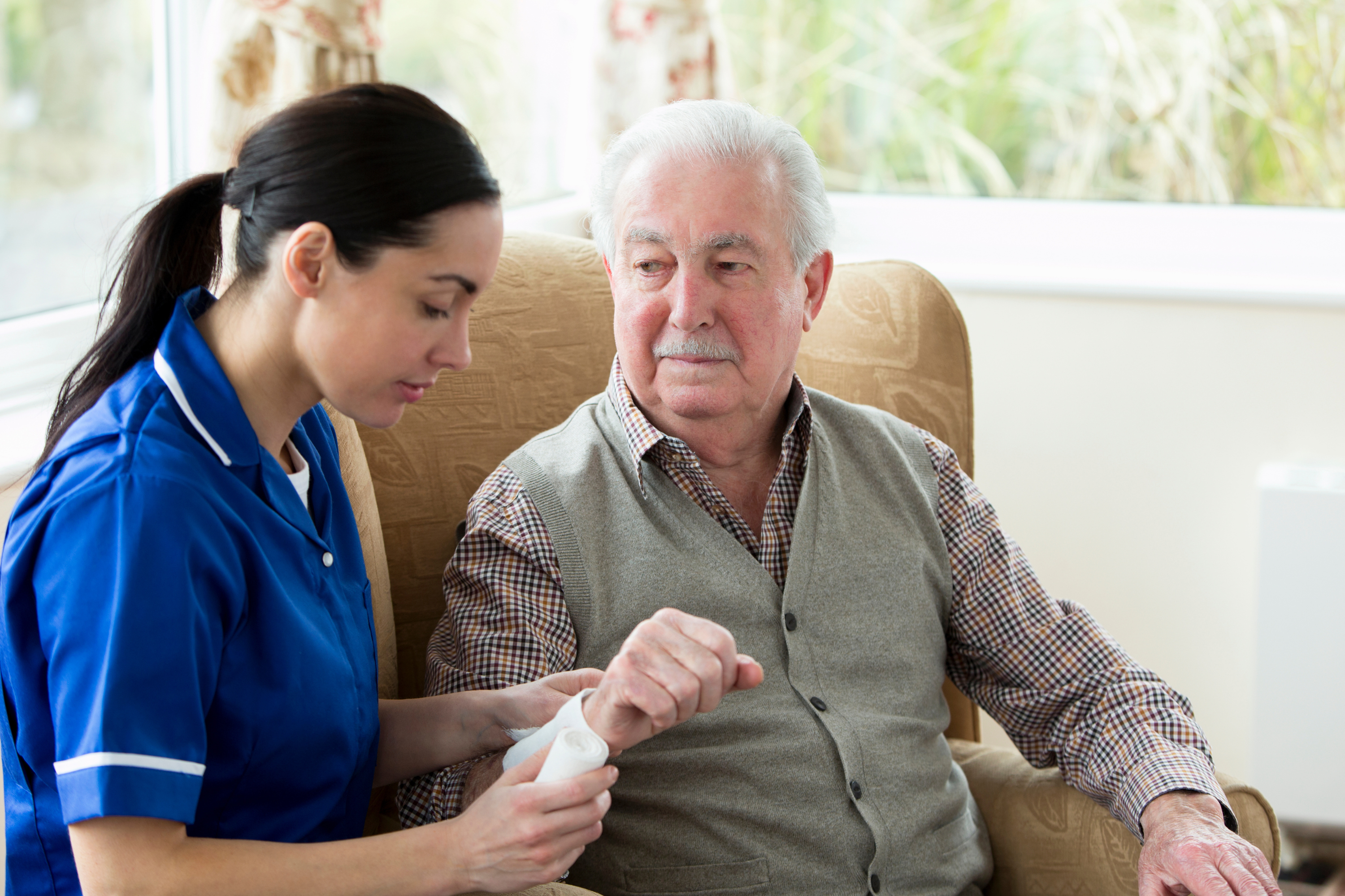 A member of care staff putting a dressing on an elderly resident's wrist.