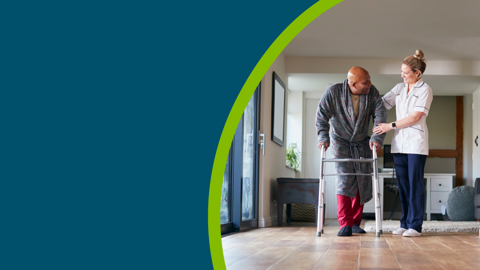 Older man in dressing gown using walking frame being helped by female care worker.