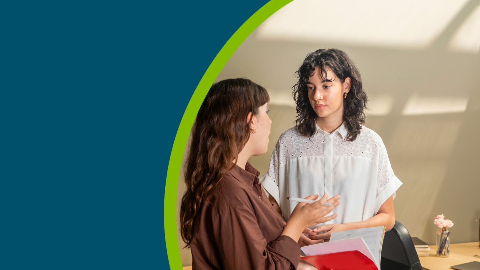 Two colleagues stood in an office setting having a meeting.