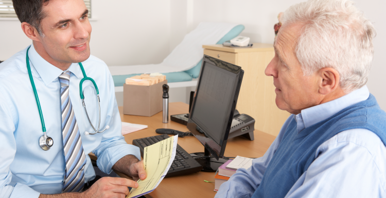 A doctor (GP) in his practice, talking with a male patient at his desk