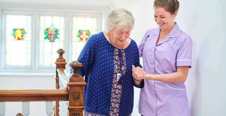 An elderly female resident being helped with her balance at the top of the stairs by a member of care staff