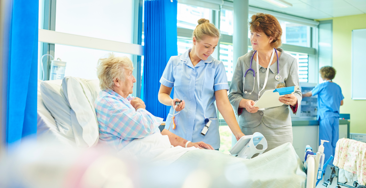 An older lady sat in a hospital bed with a nurse and doctor by her bedside