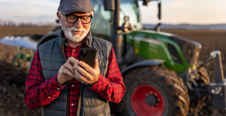 Senior farmer with mobile phone in field with tractor in background