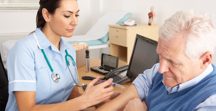 An NHS nurse giving an older man an injection at a GP practice.