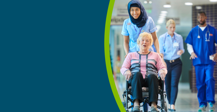 An older lady being pushed in a wheelchair down a hospital coridoor by a healthcare professional.