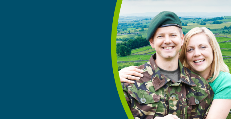 A British solider stood with his wife in the North Yorkshire countryside. Both are smiling. He is in his army uniform.