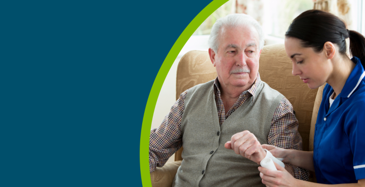 Older man having his arm bandaged in a care home by a nurse whilst he is sat down.