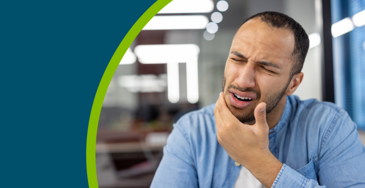 Young hispanic man suffering from a toothache sits in a modern office and grimacing, holding his hand to his cheek.