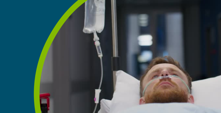 A man with an oxygen tube in his nose is lying on a trolley on a hospital corridor.