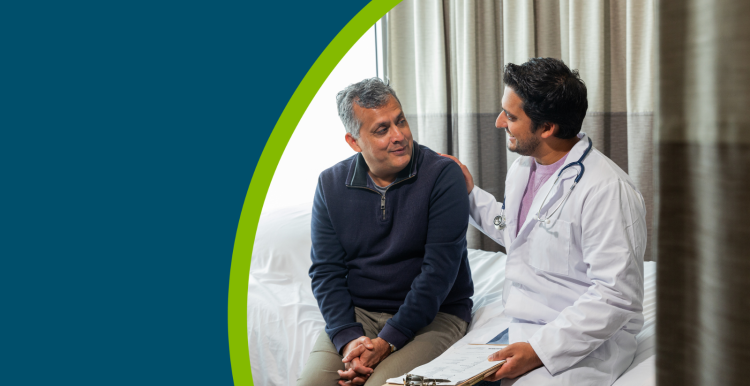 A young male doctor sitting on a hospital bed with an older male patient talking about his care.