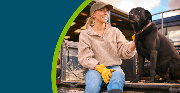 Female farm worker sitting on tailgate of off road farm vehicle with dog