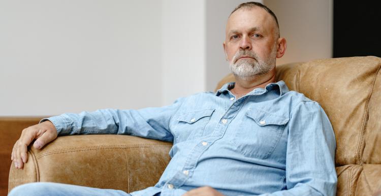 Man sits comfortably in a leather chair, wearing a denim outfit, reflecting a calm demeanor in a contemporary living space filled with natural light