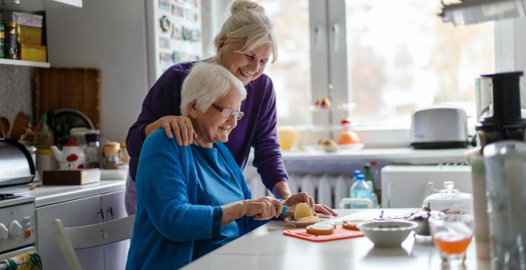 Woman spending time with her elderly mother at home whilst making lunch in the kitchen