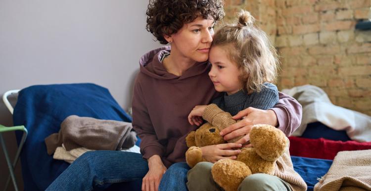Young woman giving hug to her cute little son with brown soft teddybear.