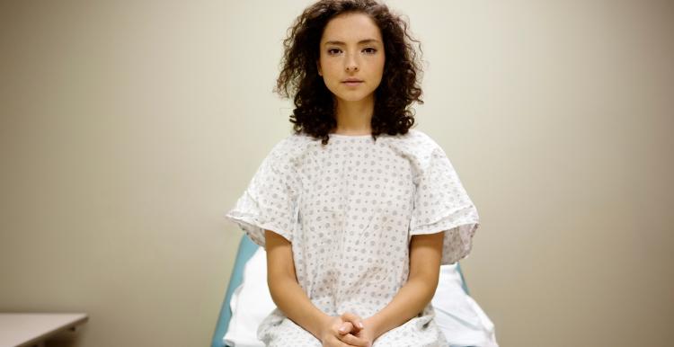 A woman sitting on a hospital bed in a hospital gown.