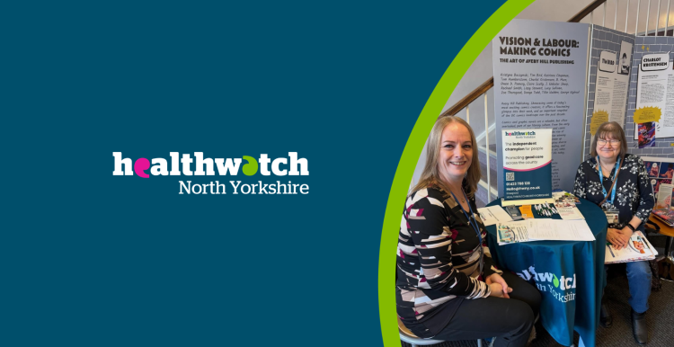 Two women sit smiling at a round table with a teal Healthwatch North Yorkshire tablecloth. The background shows a staircase with white railings and a wooden handrail.
