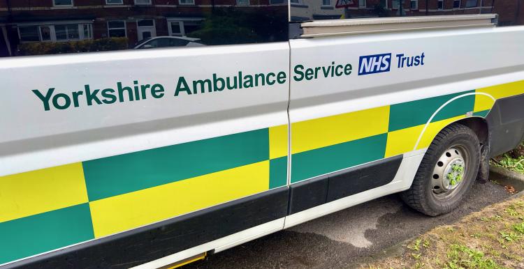 Side view of a Yorkshire Ambulance Service NHS Trust patient transport vehicle parked on a residential street