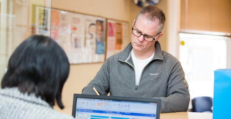 person stood at reception speaking to receptionist