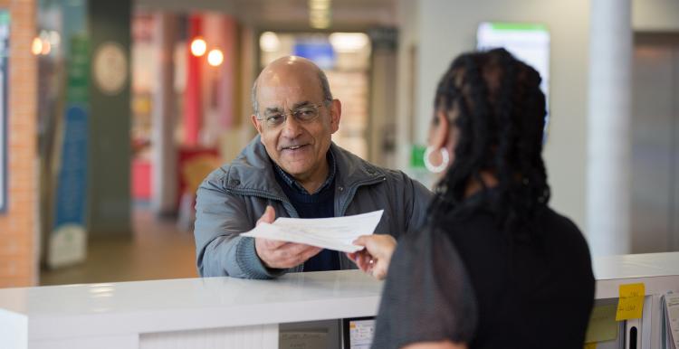 man speaking to receptionist in hospital