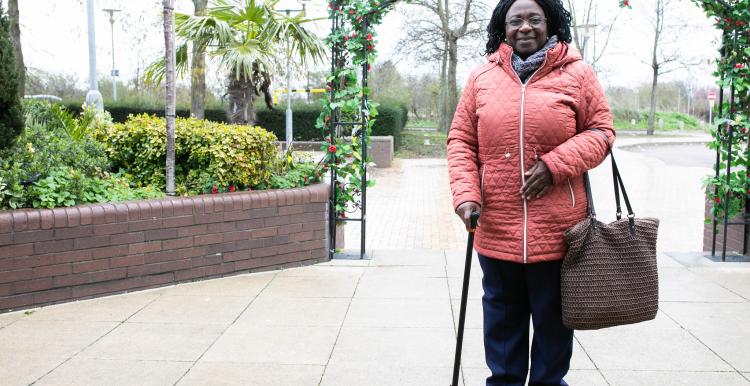 Woman stood in her coat leaning on her walking stick