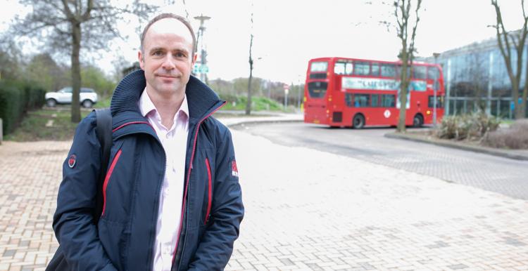 Man stood outside near a roundabout and in front of a bus