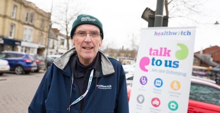Volunteer standing infront of a banner that says 'talk to us'