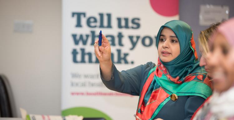 Woman in headscarf putting her hand up at Healthwatch event