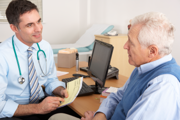 A doctor (GP) in his practice, talking with a male patient at his desk