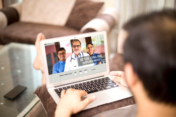 A man sat on his sofa on his laptop, booking an online GP appointment.