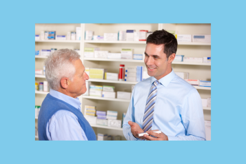 UK pharmacist serving senior man in pharmacy explaining medication.