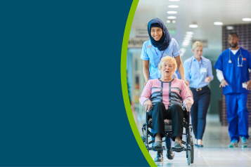 An older lady being pushed in a wheelchair down a hospital coridoor by a healthcare professional.