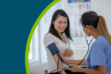 A young lady having her blood pressure taken at the doctors by a healthcare professional. She is smiling.