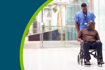 Male nurse wearing wheeling a patient in a wheelchair through a hospital lobby.