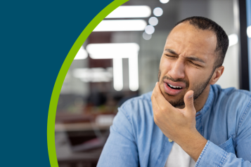Young hispanic man suffering from a toothache sits in a modern office and grimacing, holding his hand to his cheek.