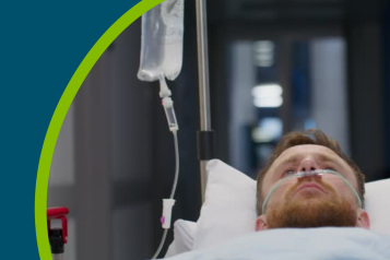 A man with an oxygen tube in his nose is lying on a trolley on a hospital corridor.