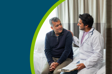 A young male doctor sitting on a hospital bed with an older male patient talking about his care.