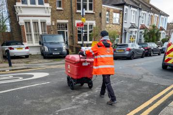 A Royal Mail postal worker on foot with a mail trolley delivering mail and parcels in a residential area.