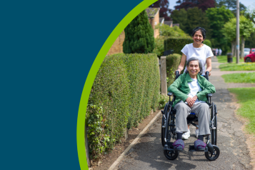 Old Indian woman in wheelchair outdoors on a pavement in a suburban street in summer