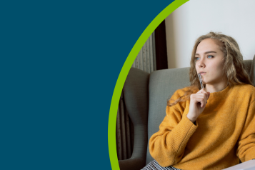 Young woman in golden yellow jumper thinking while holding a pen and notebook in a hospital waiting room