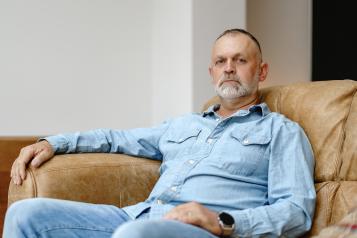 Man sits comfortably in a leather chair, wearing a denim outfit, reflecting a calm demeanor in a contemporary living space filled with natural light