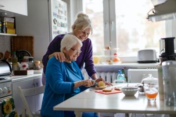 Woman spending time with her elderly mother at home whilst making lunch in the kitchen