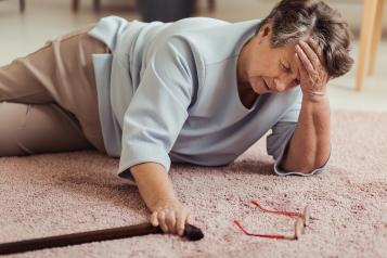 Sick older woman with headache lying on the floor with wooden stick after having a fall.