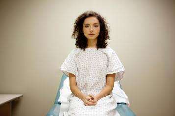 A woman sitting on a hospital bed in a hospital gown.