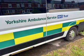 Side view of a Yorkshire Ambulance Service NHS Trust patient transport vehicle parked on a residential street