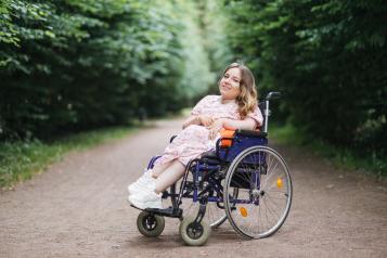 Young lady with spinal muscular atrophy spending warm summer day on fresh air. 