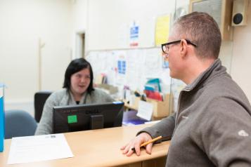 man speaking to receptionist at GP