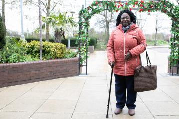 Woman stood in her coat leaning on her walking stick