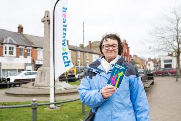 Lady at an outdoor Healthwatch event, holding a leaflet and ready to engage